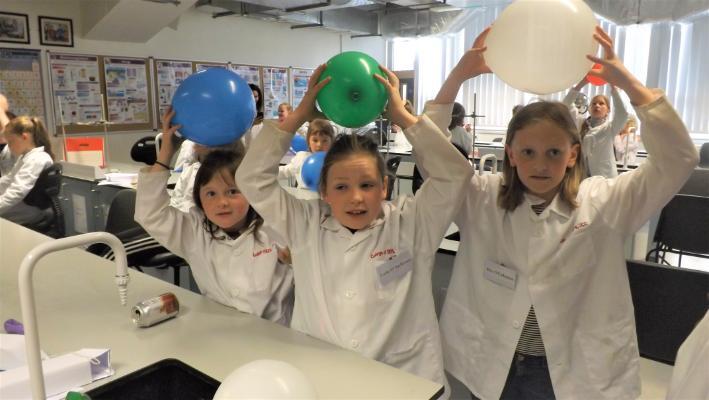 Three girls using balloons to create static electricity which pulls the hair up