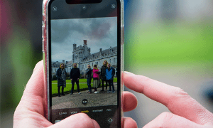 Close up of hands holding phone while taking a photo of students on Quad
