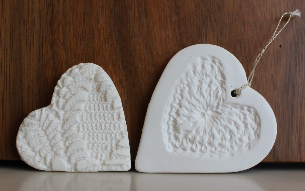 Two ceramic hand-made hearts lying on their side facing each other against a wooden background