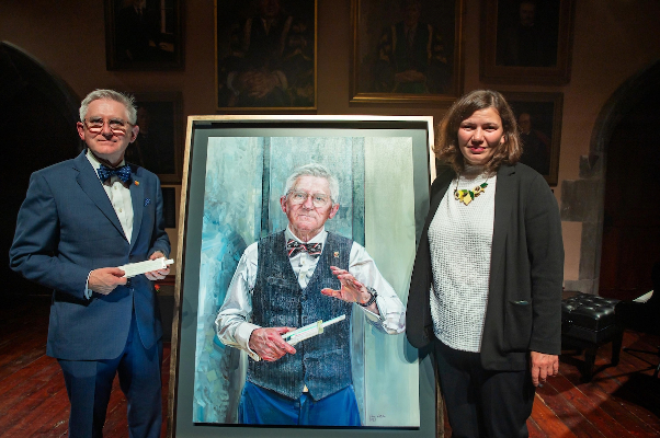 Professor Patrick O'Shea stands with artist Vera Klute by his portrait in the Aula Maxima, UCC. Image credit: John Allen.