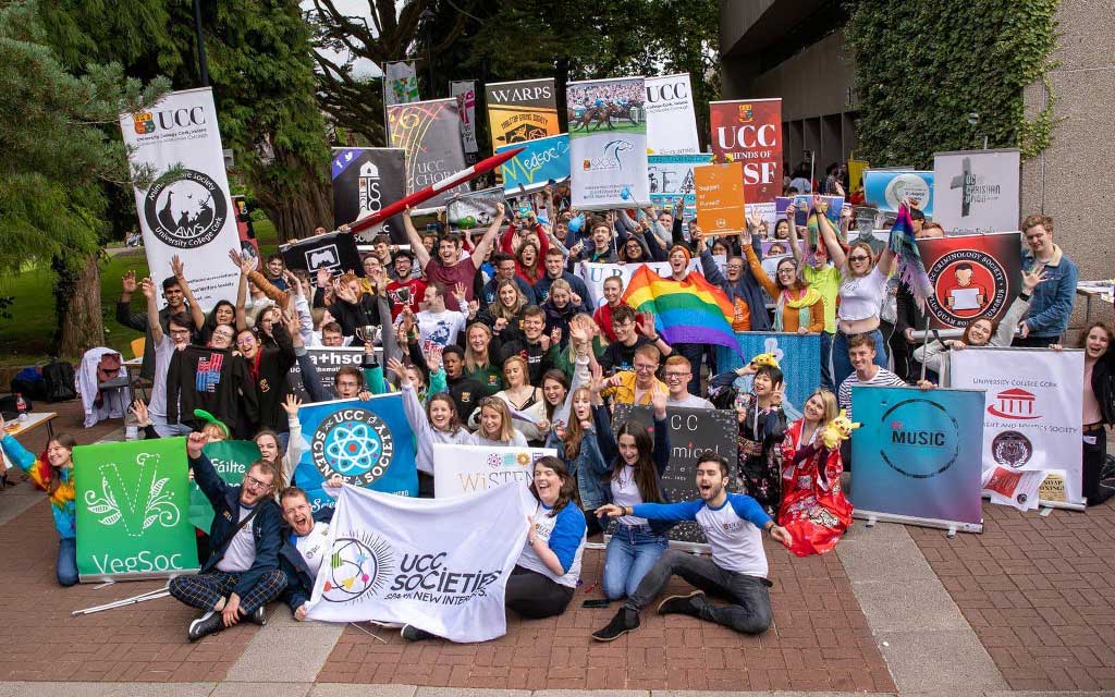 Dozens of UCC students gather on campus with banners representing various UCC student societies