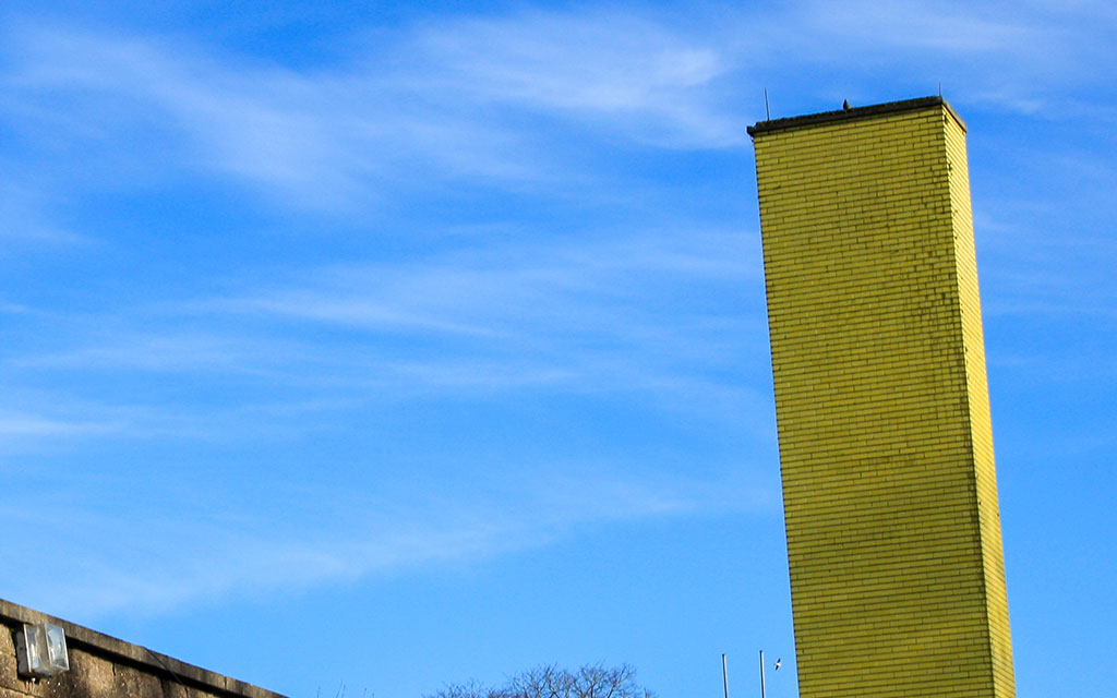 A view of the yellow tiled chimney rising above the old bottling plant on Distillery Fields under a blue sky with minimal cloud cover