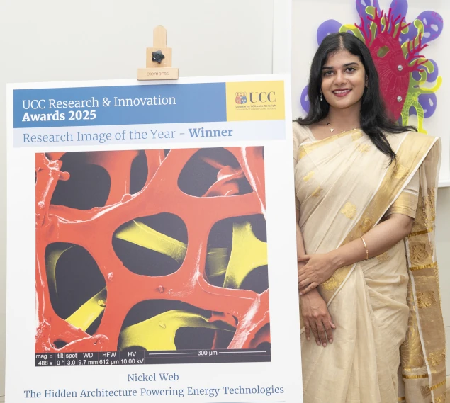 Dr Rupa Ranjani poses next to a large print of her award-winning scientific image, a colourful microscopic lattice scaled large.