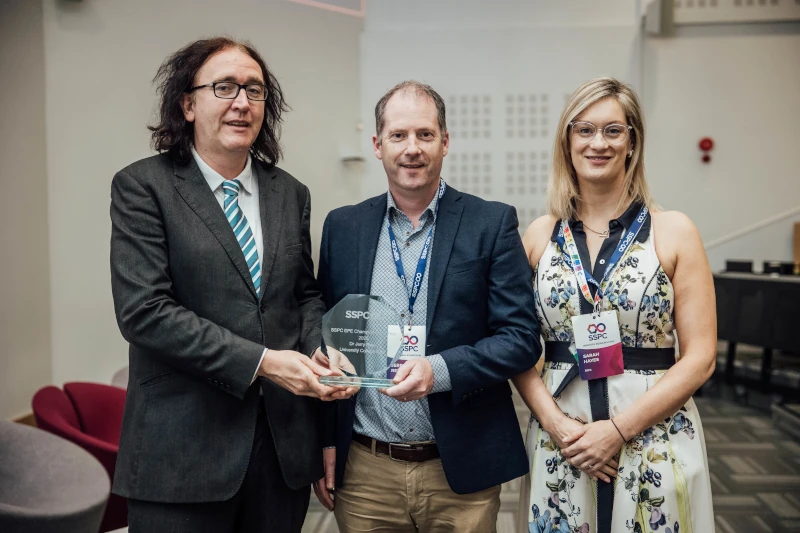 Dr Jerry Reen poses while accepting an award, flanked on either side by two other people. Dr Jerry Reen poses while accepting an award, flanked on either side by two other people.