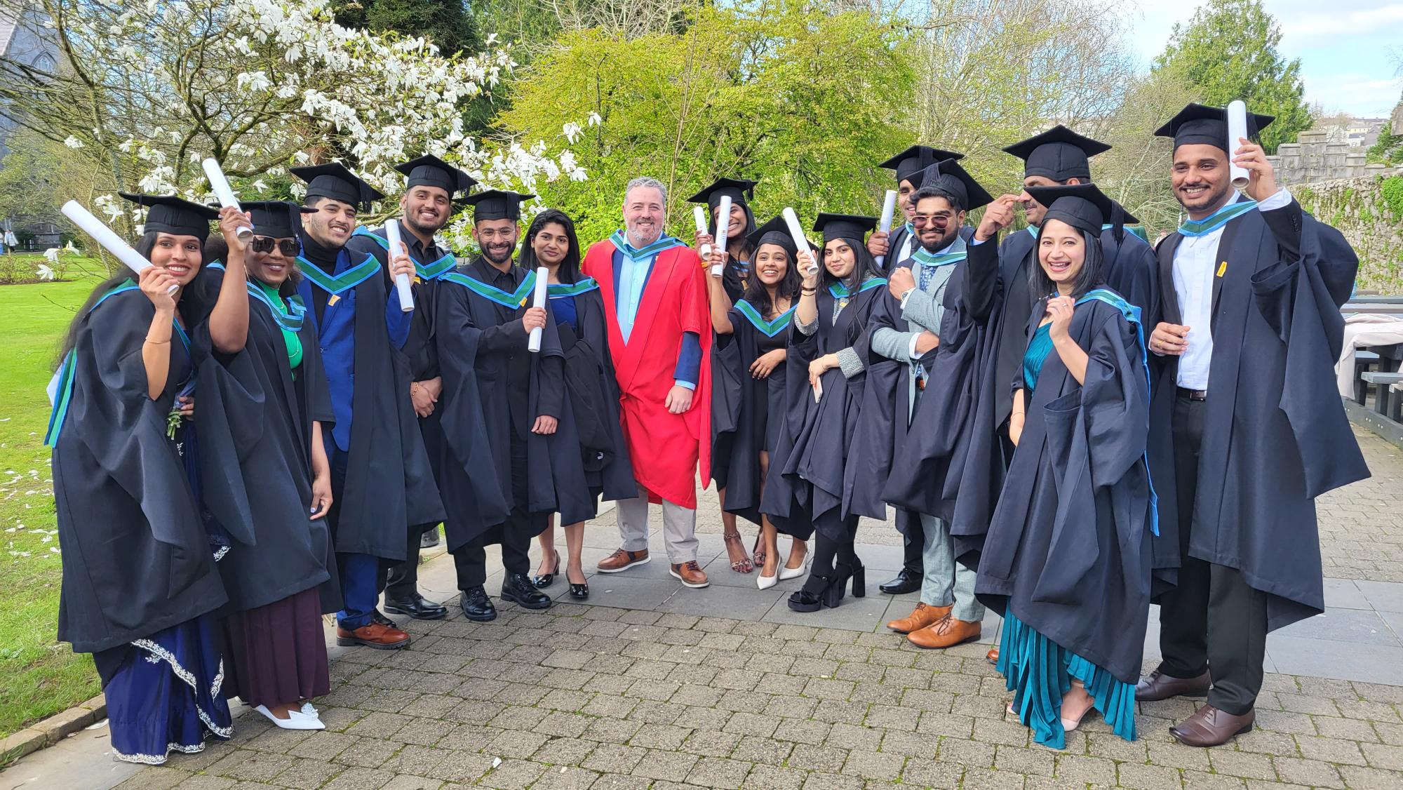 A group of MSc graduates in gowns with their supervisor.