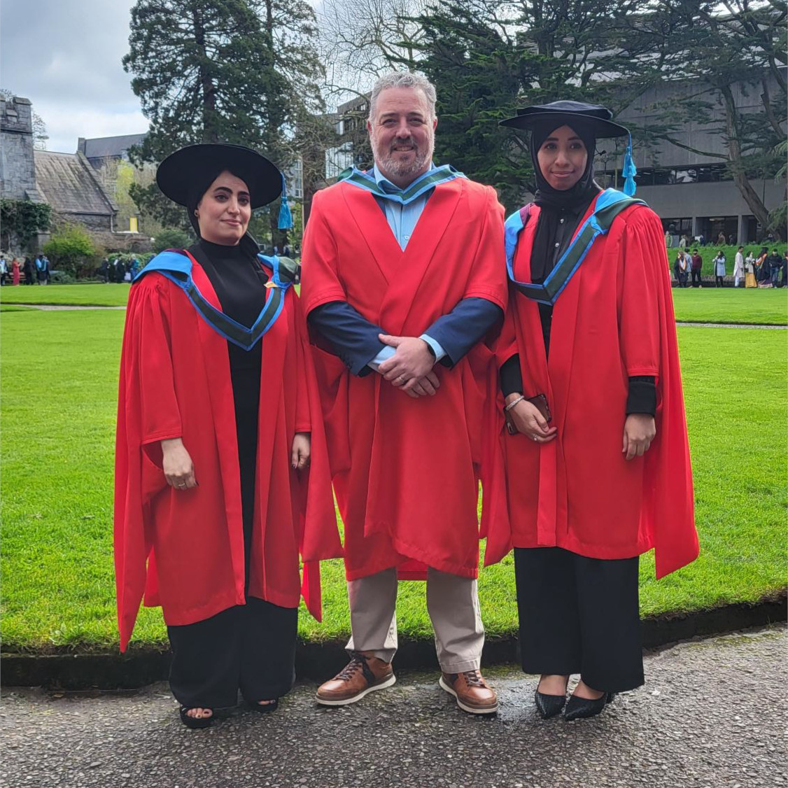 Two PhD graduates in robes with their supervisor at UCC Quad.