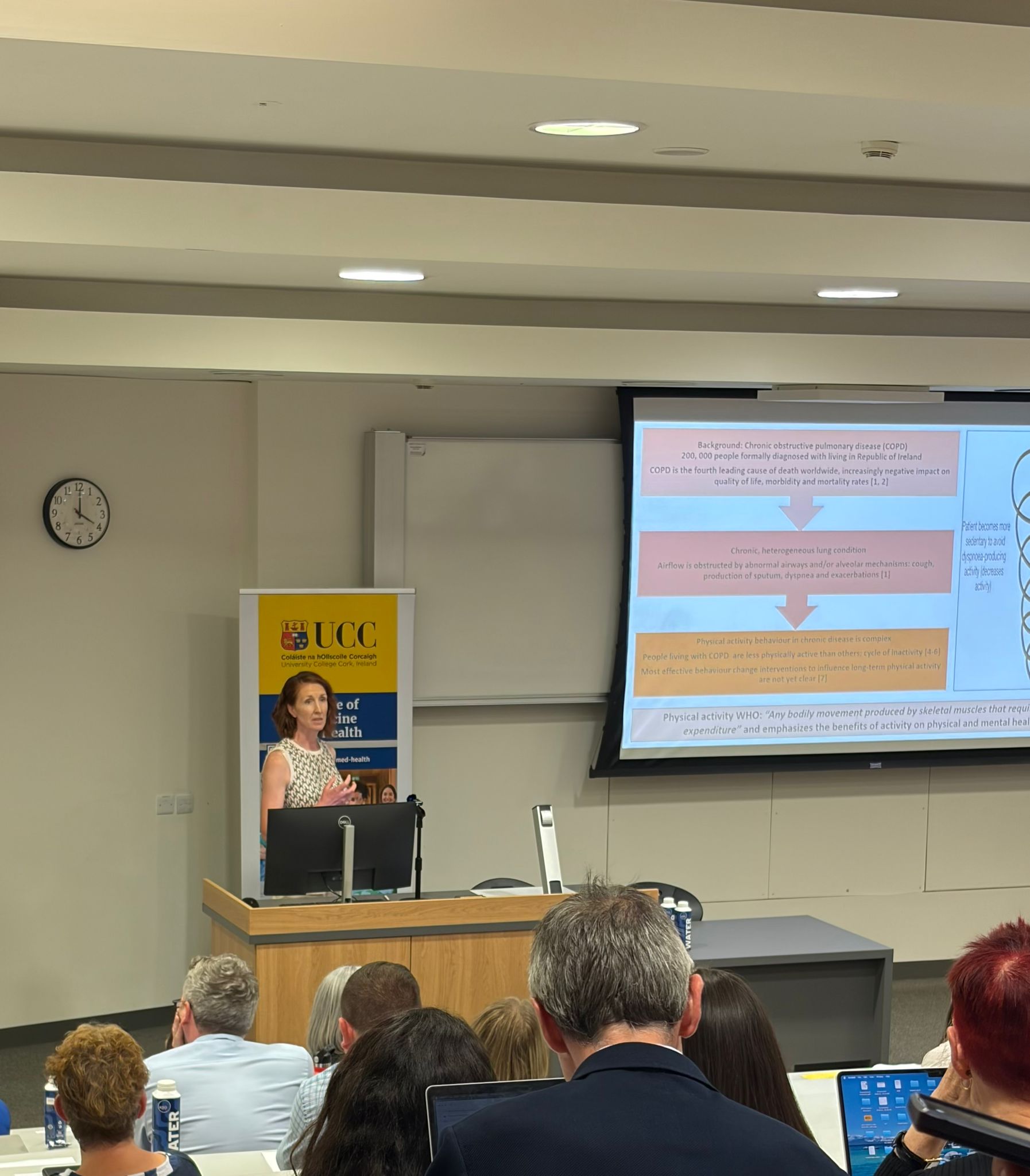 Ciara Hanrahan presenting at a podium with the preesentation behind her and a seated audience infront