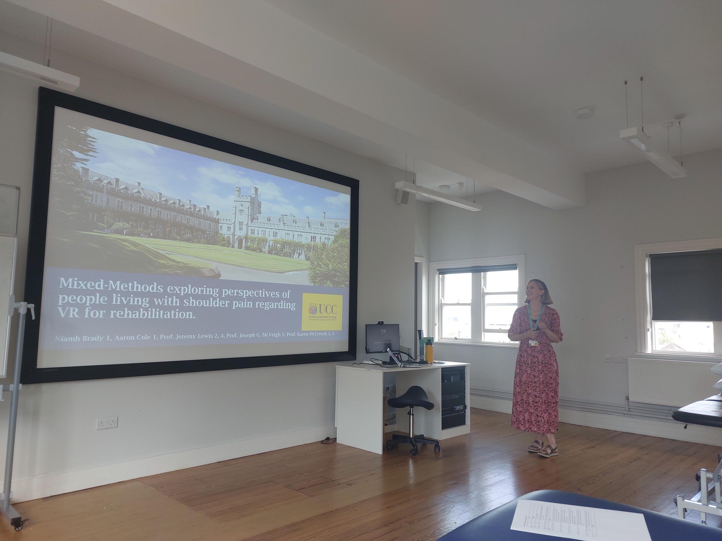 Niamh Brady standing infront of a wall where a power point presentation is being displayed Niamh Brady standing infront of a wall where a power point presentation is being displayed