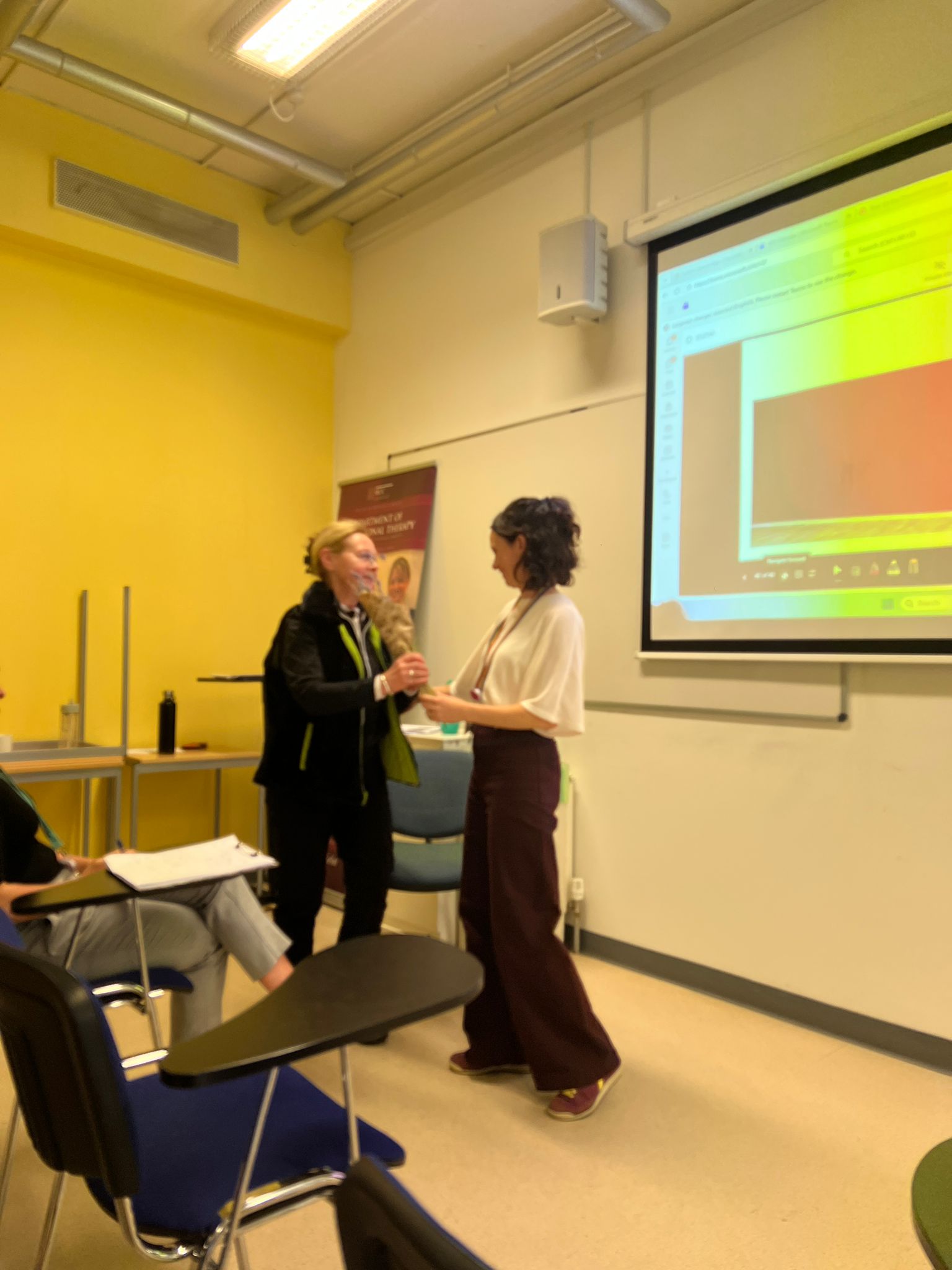 Female being given an award by another female in a classroom setting Female being given an award by another female in a classroom setting