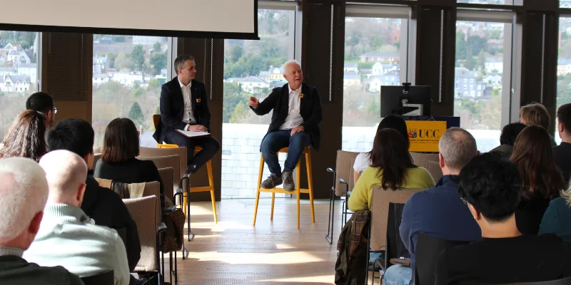 Image of two men seated talking to a crowd Image of two men seated talking to a crowd