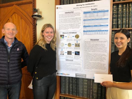 Best Poster 2022-23 winners Antibiotics Unearthed, Niall O’Leary presenting and Beth Callaly and Louisa Faherty McGrath receiving their prize.