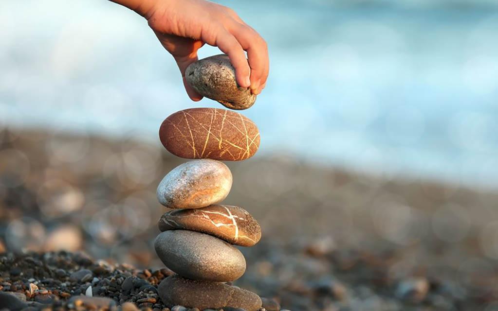 An image of a hand creating a stack of rock on a stony beach