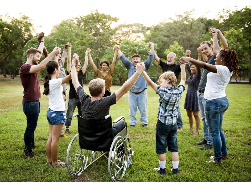 A diverse group of people are in a circle outdoors. They are holding hands