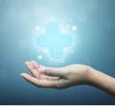 A hand holds a floating blue medical cross against a luminous blue background