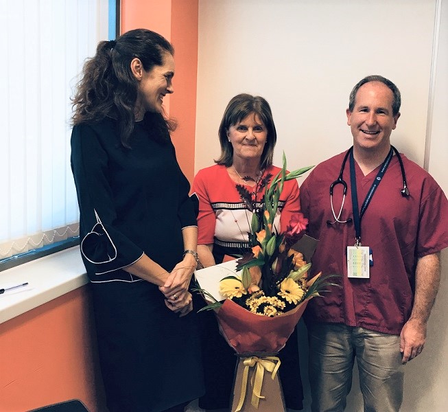 3 people standing together with 1 holding a bunch of flowers