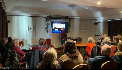 Professor given talk, screen showing presentation and those in attendance sitting facing screen with backs to the camera