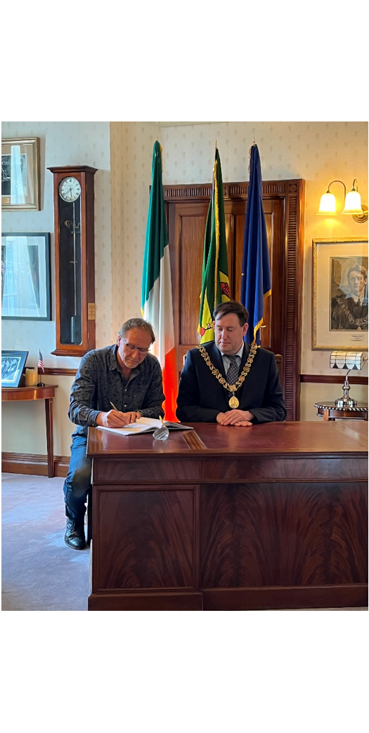 Visitor signing visitors book UCC with Lord Mayor, desk and flags in background