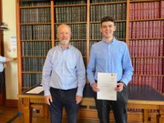 Student holding cert with lecturer next to him (book backdrop)