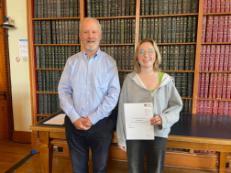 Student with cert along side lecturer (book backdrop)