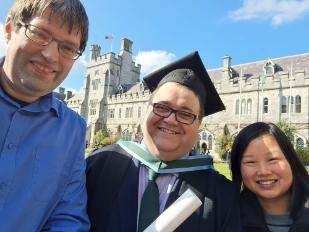 conferring on UCC quad, 2 people in photo, one with gown and scroll