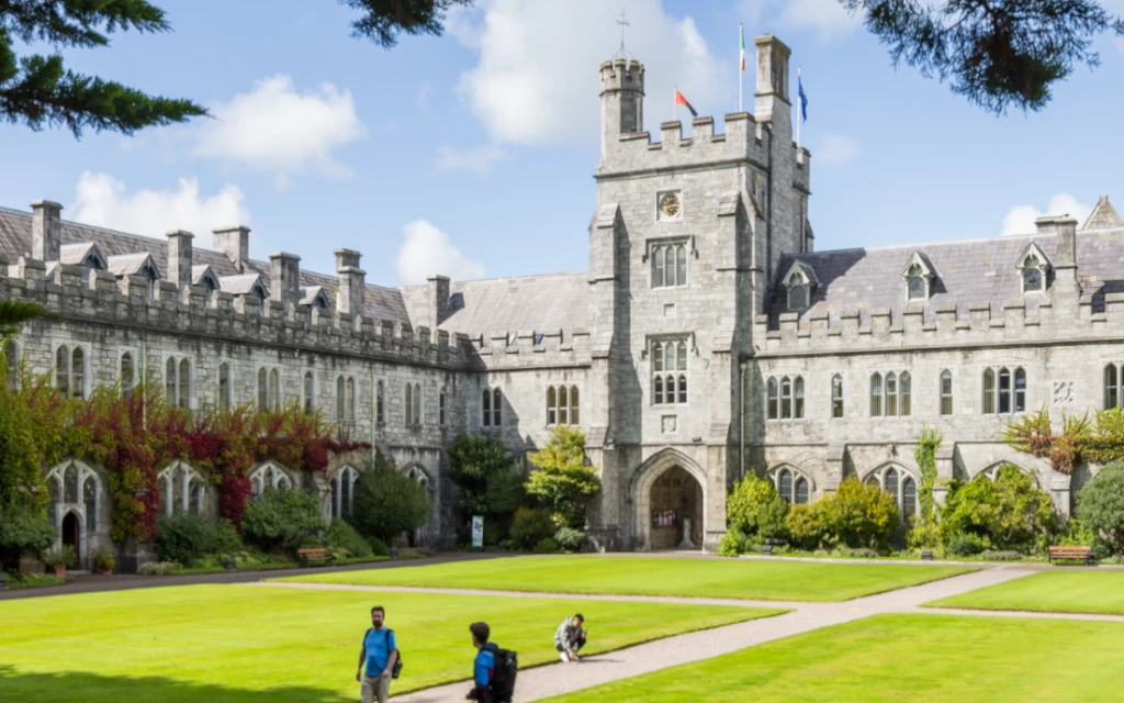 Image of the UCC quad on a sunny day with people strolling around it