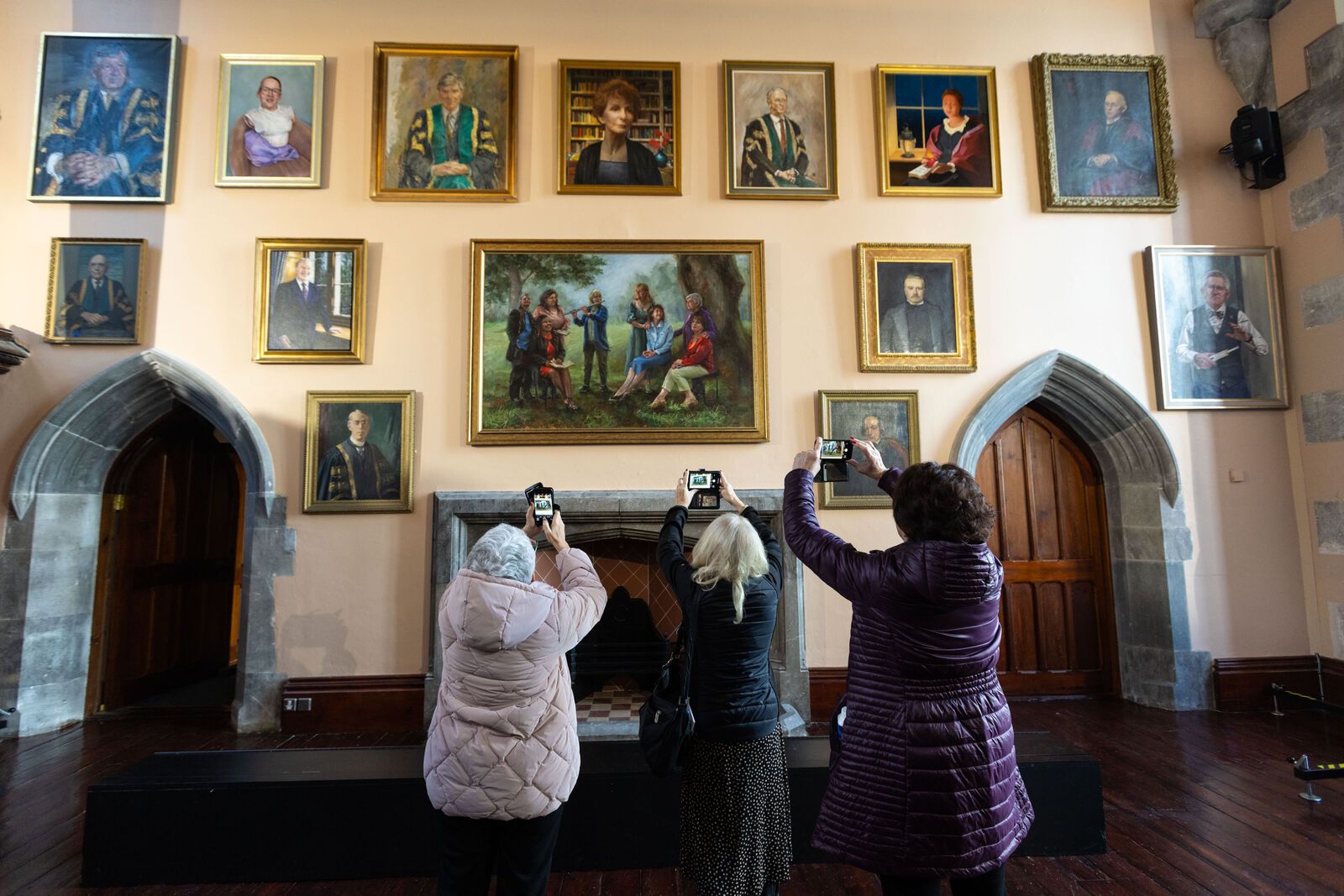 three women take photographs of the newly unveiled portraits in the Aula Maxima