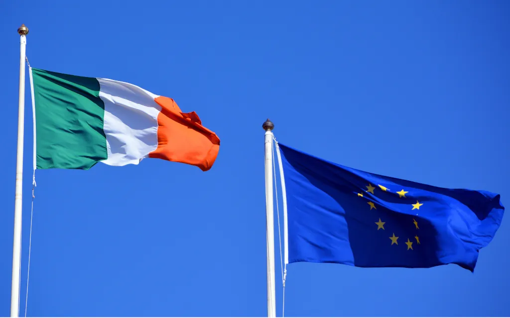 Irish and EU Flags fly from flag poles against a blue background