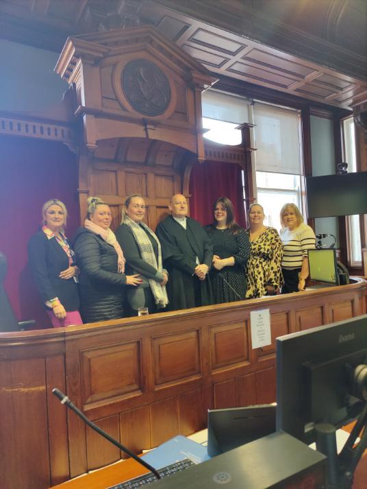 A group of women stand with a judge at the bench, all are smiling