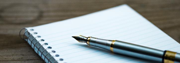 A fountain pen lying on a blank page of a lined spiral notebook