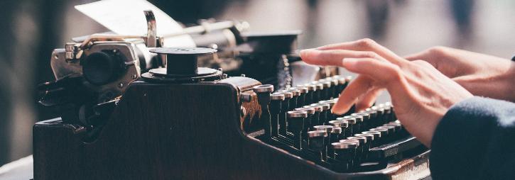 An old-fashioned typewriter, with two typing hands and a sheet of paper sticking out