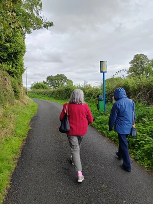 Two people walking along a wet road surrounded by green vegetation Two people walking along a wet road surrounded by green vegetation