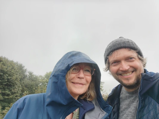 Two people walking outdoors in the rain smile into a camera Two people walking outdoors in the rain smile into a camera