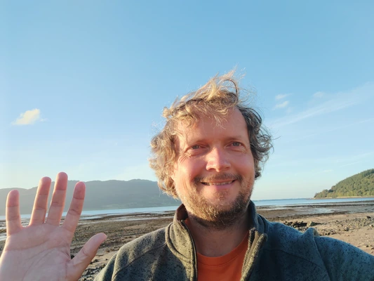 A smiling person waves towards the camera against a blue sky background A smiling person waves towards the camera against a blue sky background