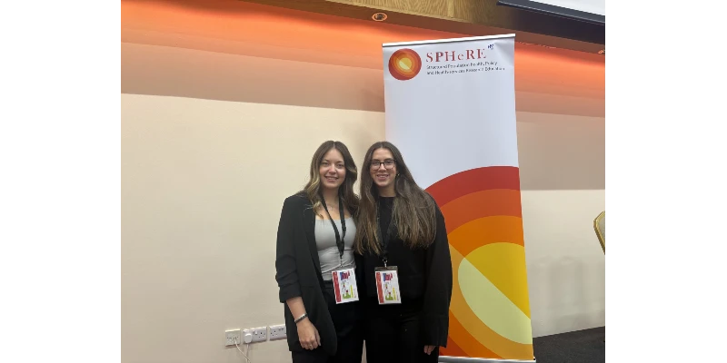 2 young females in black smiling underneath a SPHeRE banner