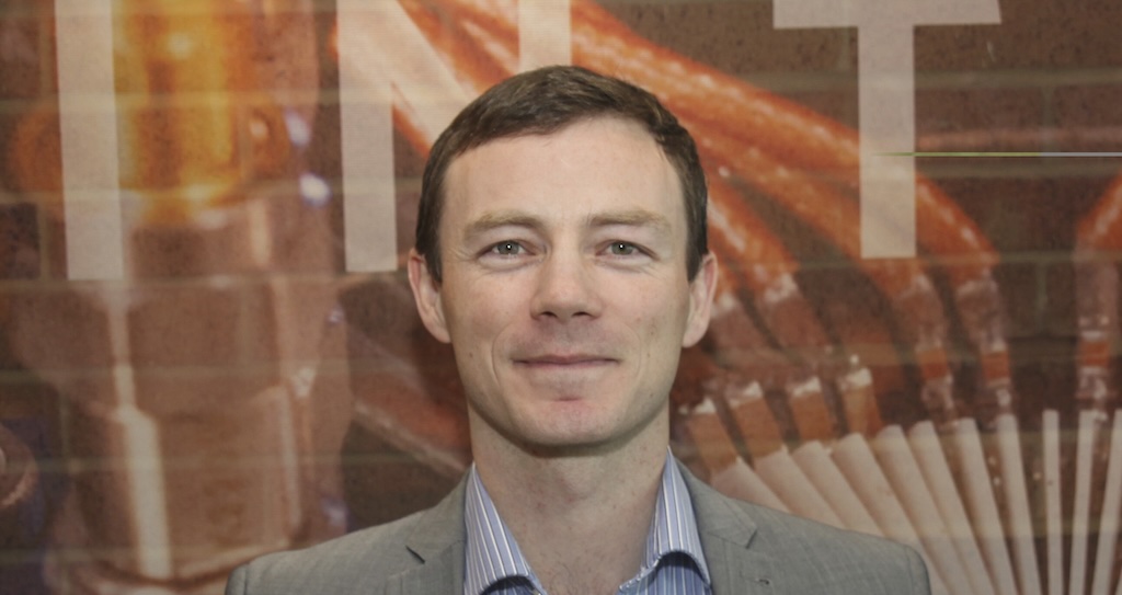 a picture of a smiling man with a blue shirt and beige jacket