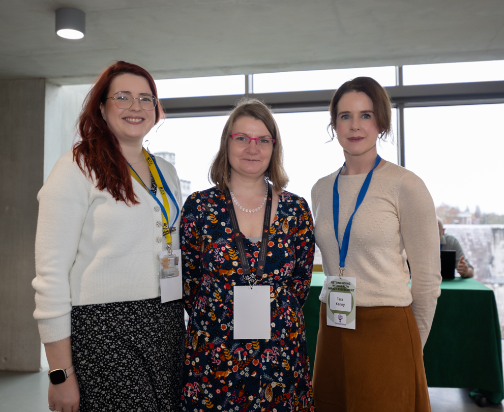 Three women at a conferenc, smiling and facing the camera
