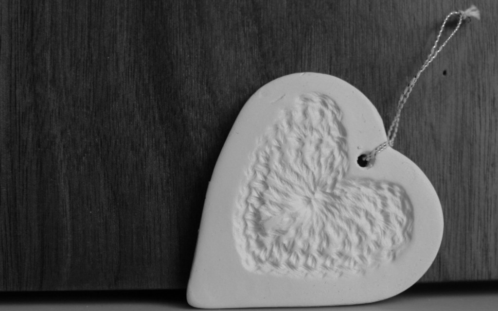 black and white image of a white ceramic heart lying on its side on a cream surface against a wooden background
