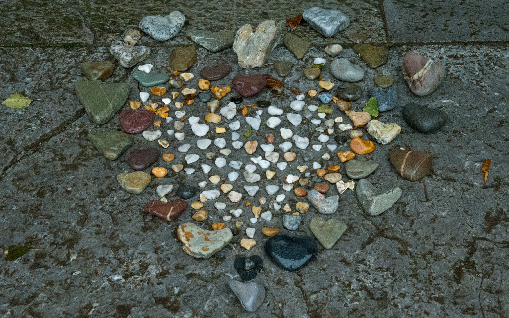 Coloured stones of different sizes in a heart shape on the ground (dark grey)