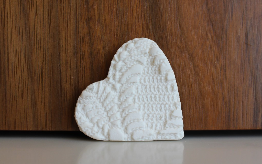 white ceramic heart lying on its side on a cream surface against a wooden background