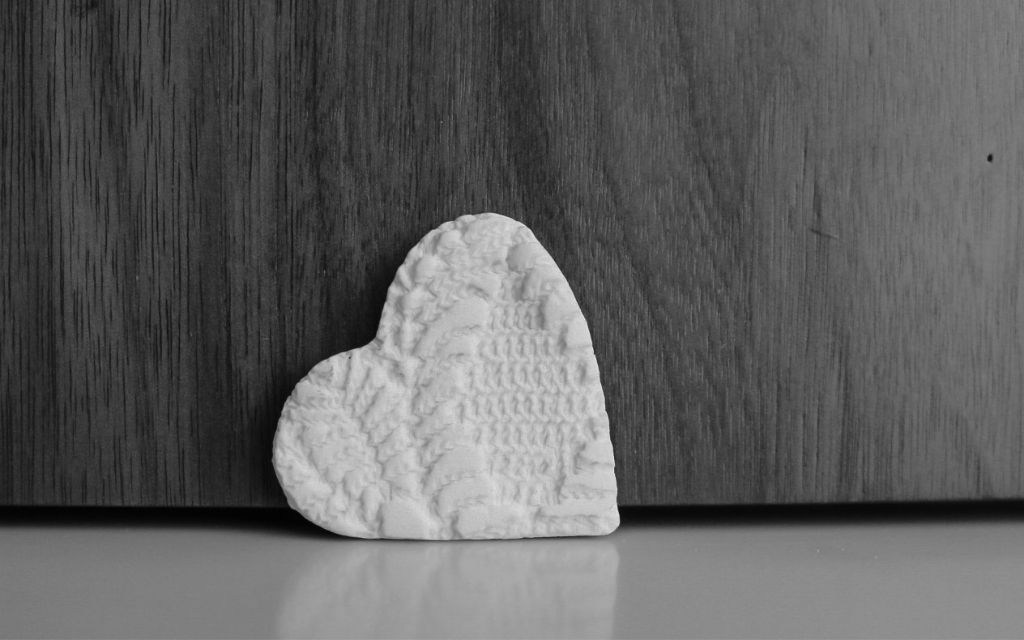 white ceramic heart lying on its side on a cream surface against a wooden background, black & white