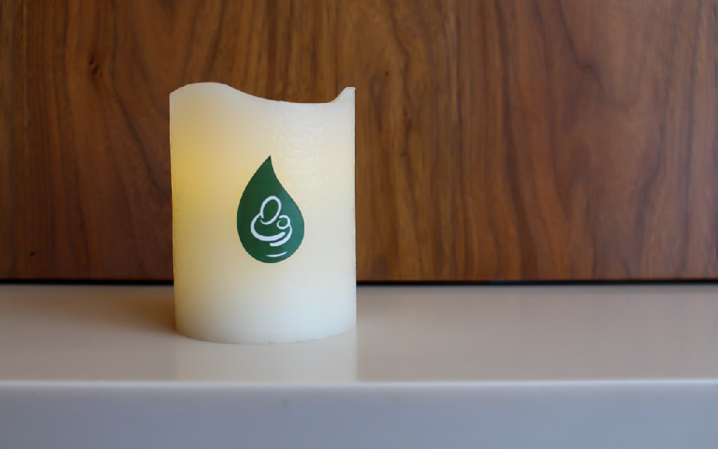 white pillar candle with the PLRG logo on it sitting on a cream surface against a wooden background