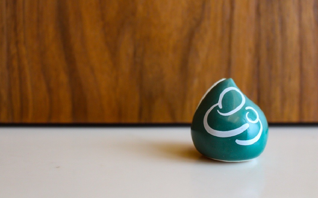 green ceramic teardrop-shaped photo holder with white outline of person holding baby, on a cream surface against a wooden background