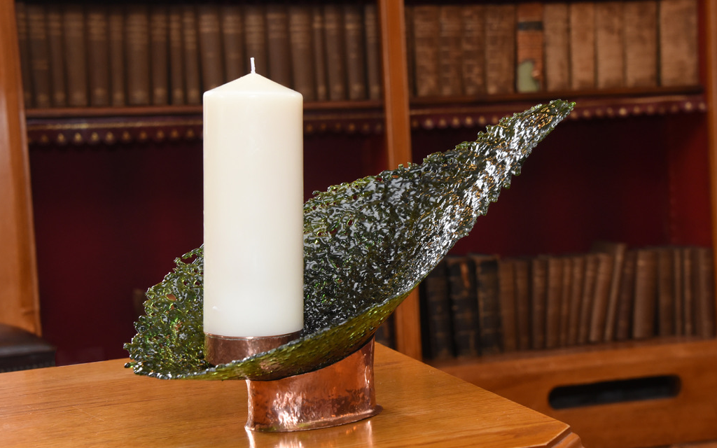 image of an ivory candle in a moss green leaf-shaped piece of artwork on a wooden table with bookcase in background