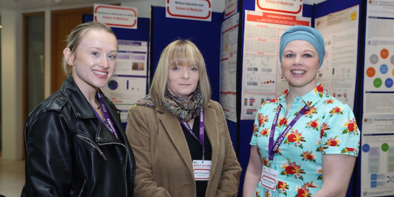 Three women standing for a photograph, poster boards in the background