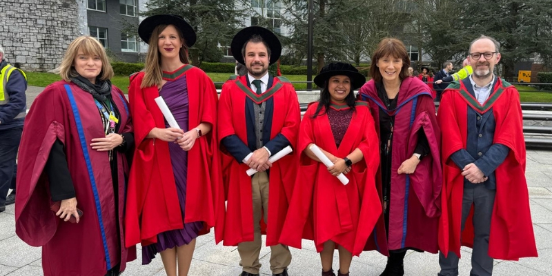 Six people (standing) in red robes on graduation day