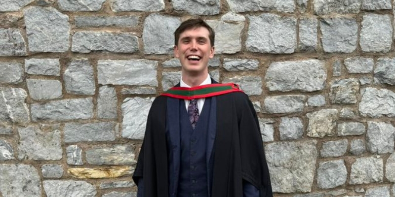 Man standing in a graduation robe, smiling