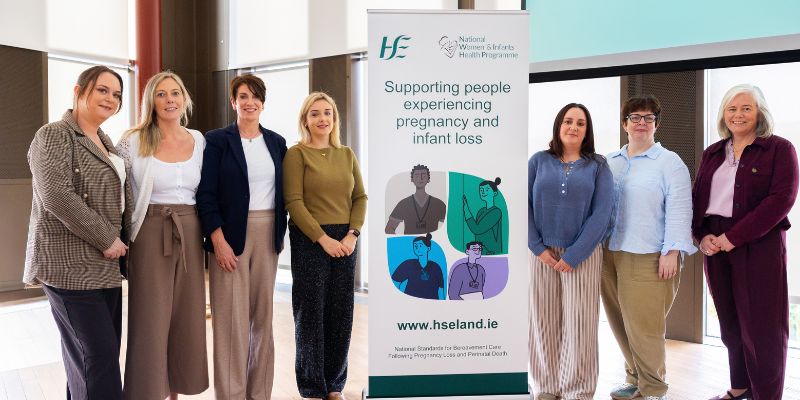 Group of 7 women, standing, with a pull up banner in the middle of the row of them. The banner is advertising an e-learning programme on supporting people experiencing pregnancy and infant loss Group of 7 women, standing, with a pull up banner in the middle of the row of them. The banner is advertising an e-learning programme on supporting people experiencing pregnancy and infant loss