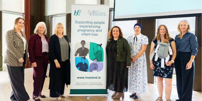 Group of 7 women, standing, with a pull up banner in the middle of the row of them. The banner is advertising an e-learning programme on supporting people experiencing pregnancy and infant loss Group of 7 women, standing, with a pull up banner in the middle of the row of them. The banner is advertising an e-learning programme on supporting people experiencing pregnancy and infant loss