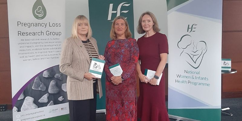 Three women standing, each holding an A5 booklet