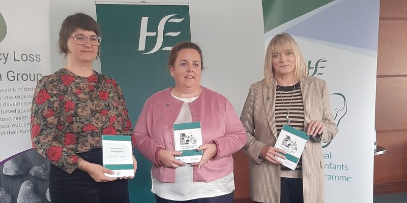 Three women standing, each holding an A5 booklet